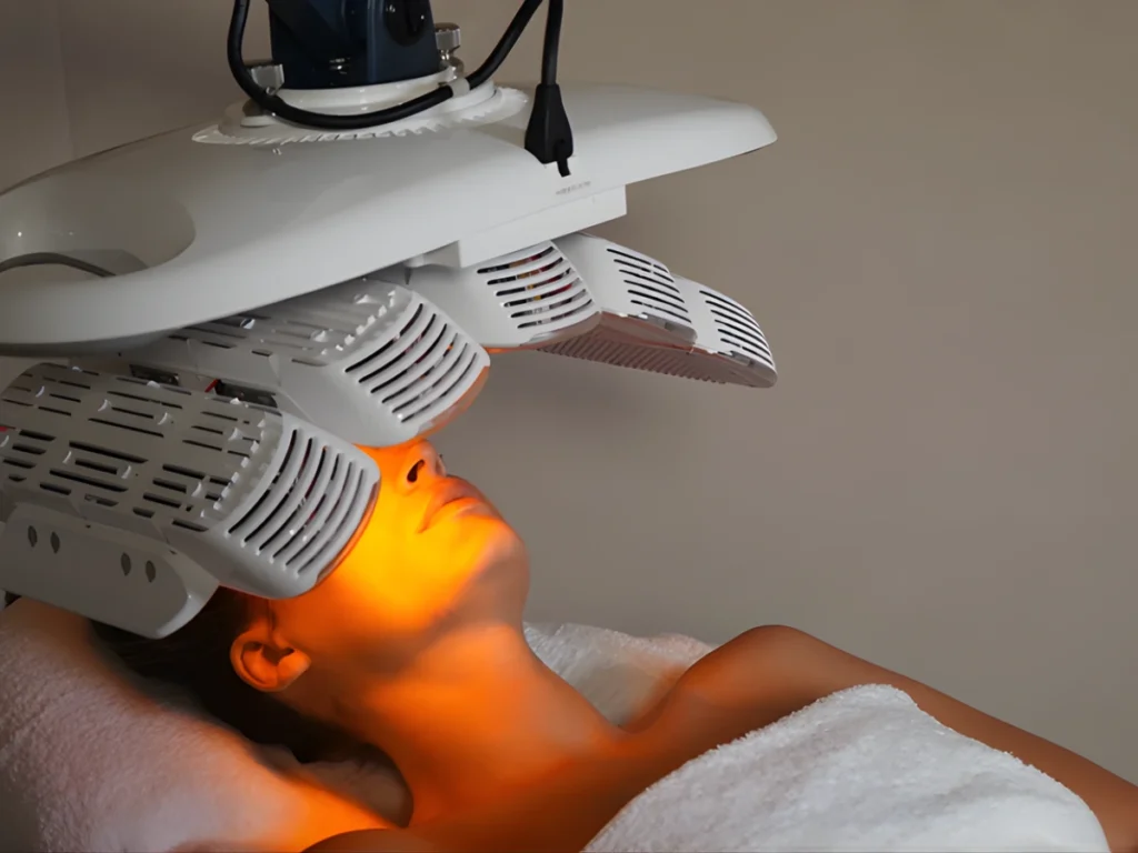Person receiving LED light therapy facial treatment under a Healite II device at a spa clinic